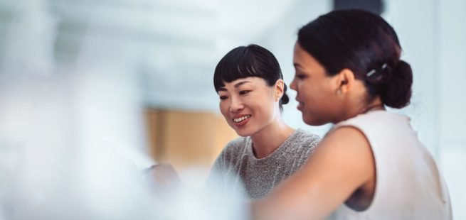 Two professional women engaged in a collaborative discussion in a modern office setting. Concept of teamwork, business, and office communication.
